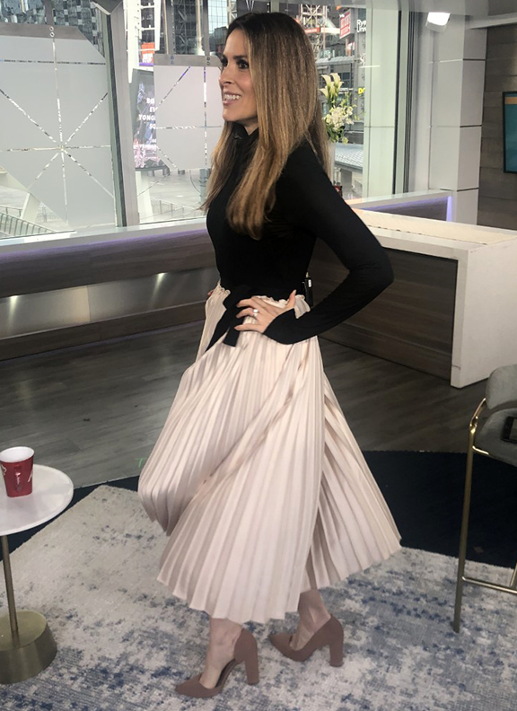 Dina wearing beige pleated skirt with black turtle neck